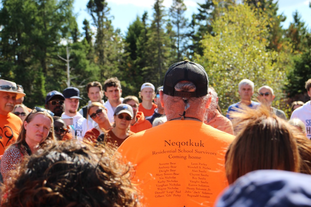 a crowd of people highlighting the back of one man's bright orange shirt in rememberance of First Nation citizens impacted by forced integration