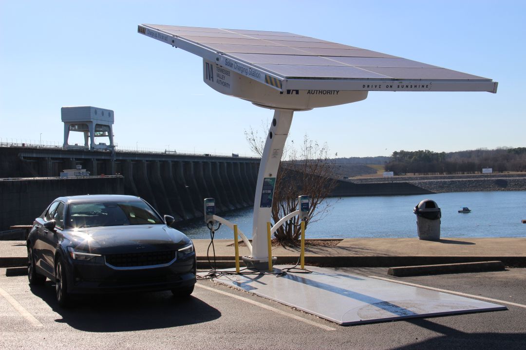 electric vehicle plugged into a solar panel in front of a hydro-electric dam